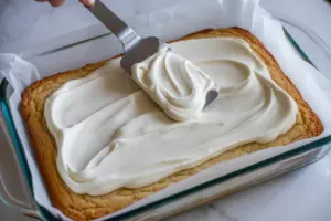 . Spread thick white frosting evenly over cooled sugar cookie bars with spatule