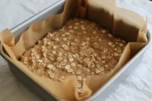 8×8-inch white baking pan with brown parchment paper filled with Maple Cinnamon Sourdough Oatmeal Breakfast Bars